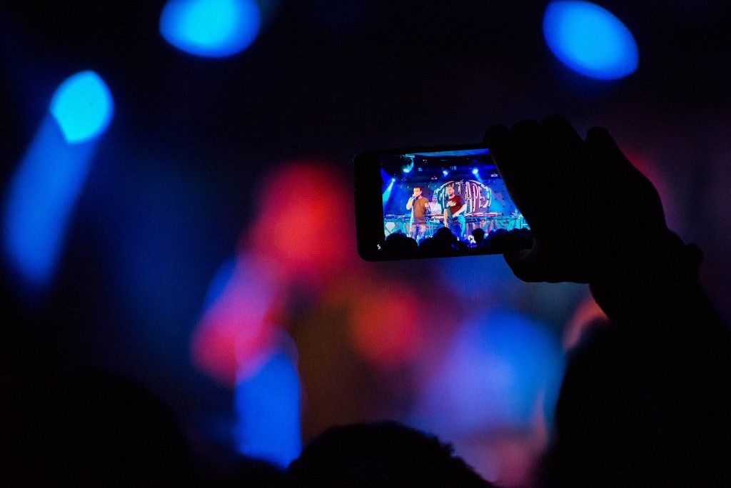 Concert crowd filming the stage on a phone, MIXTAPE backdrop visible on screen