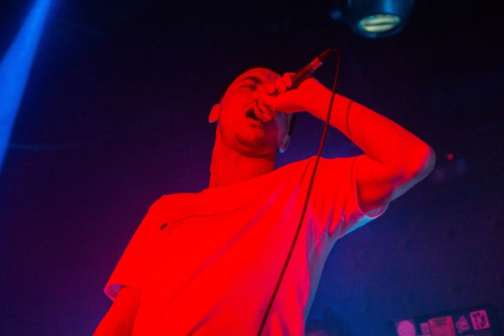 Performer singing into a microphone under red and blue stage lighting
