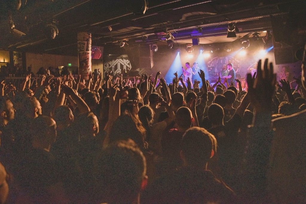 Crowd at a live hip-hop concert with hands raised toward the stage